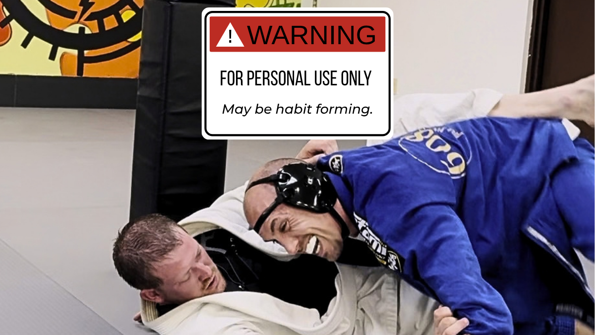 Two jiu jitsu practitioners grappling, one grinning, beneath a sign reading “Warning: For Personal Use Only. May be habit formed.”