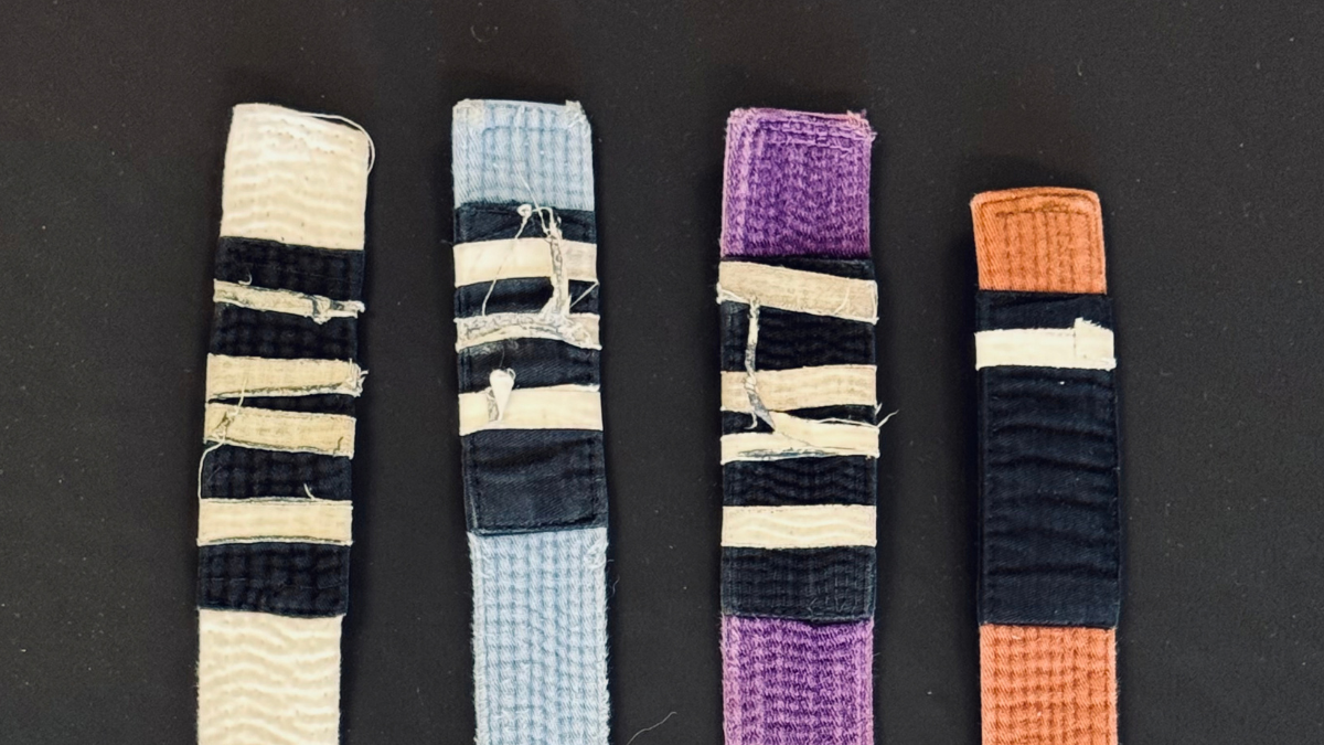 Worn jiu jitsu belts with taped stripes arranged side by side on a dark background.