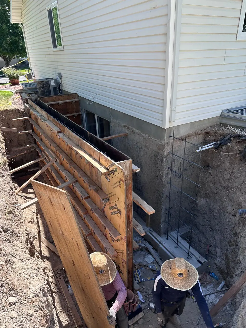 Crew assembling concrete wall forms and reinforcement beside a home