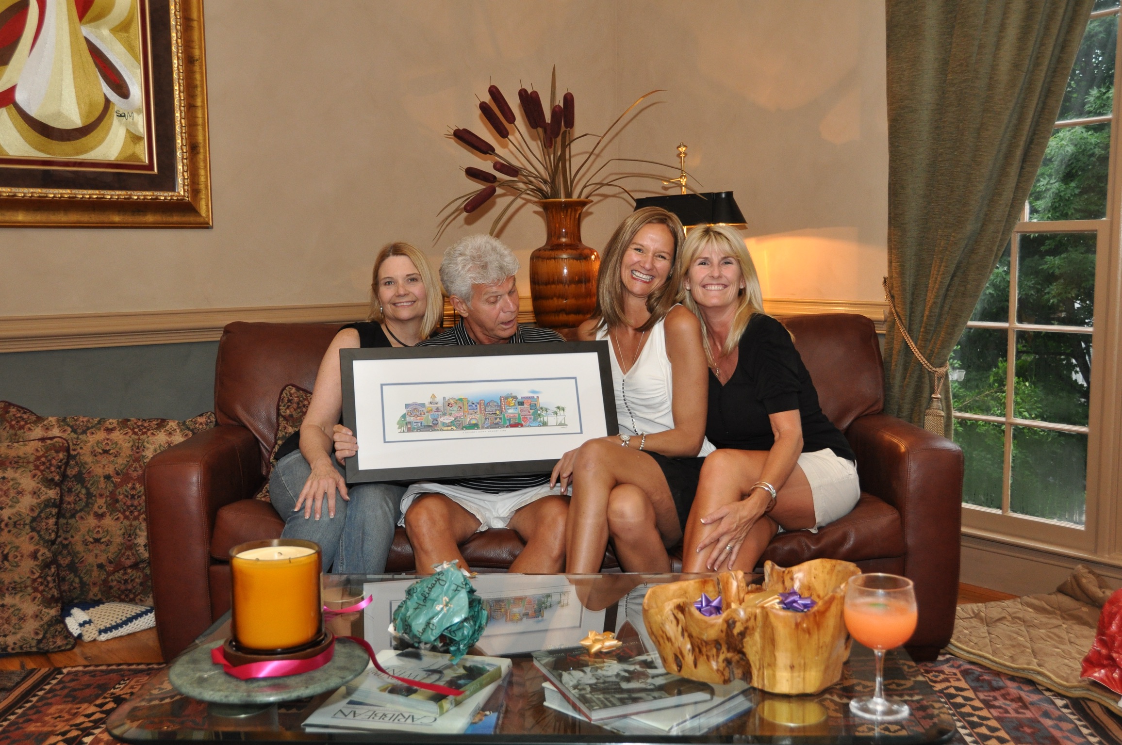 Two families on a couch holding their framed Your Memory Lane 8-building wedding street print.