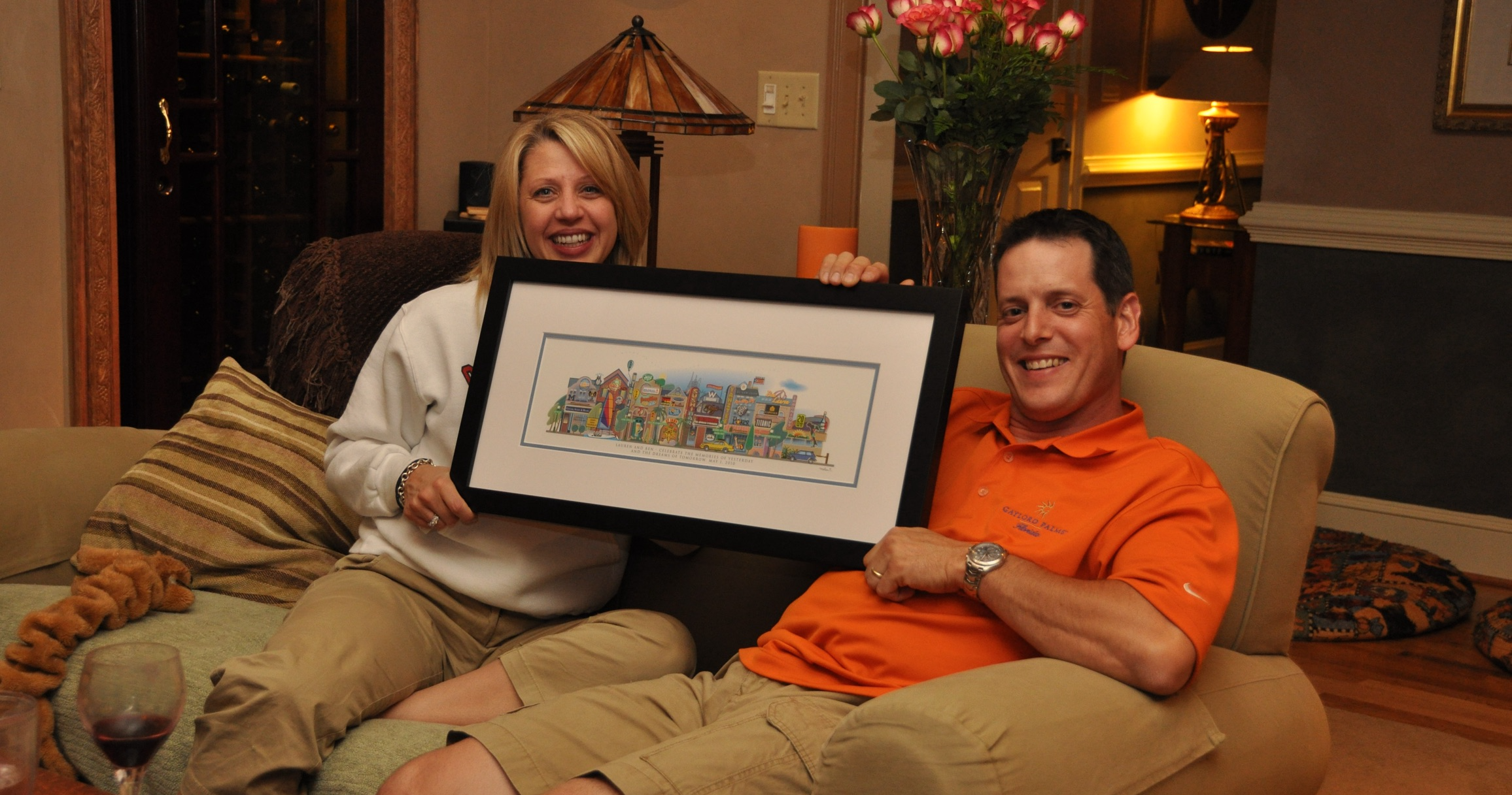 A couple on the couch holding their framed Your Memory Lane first-anniversary street print.