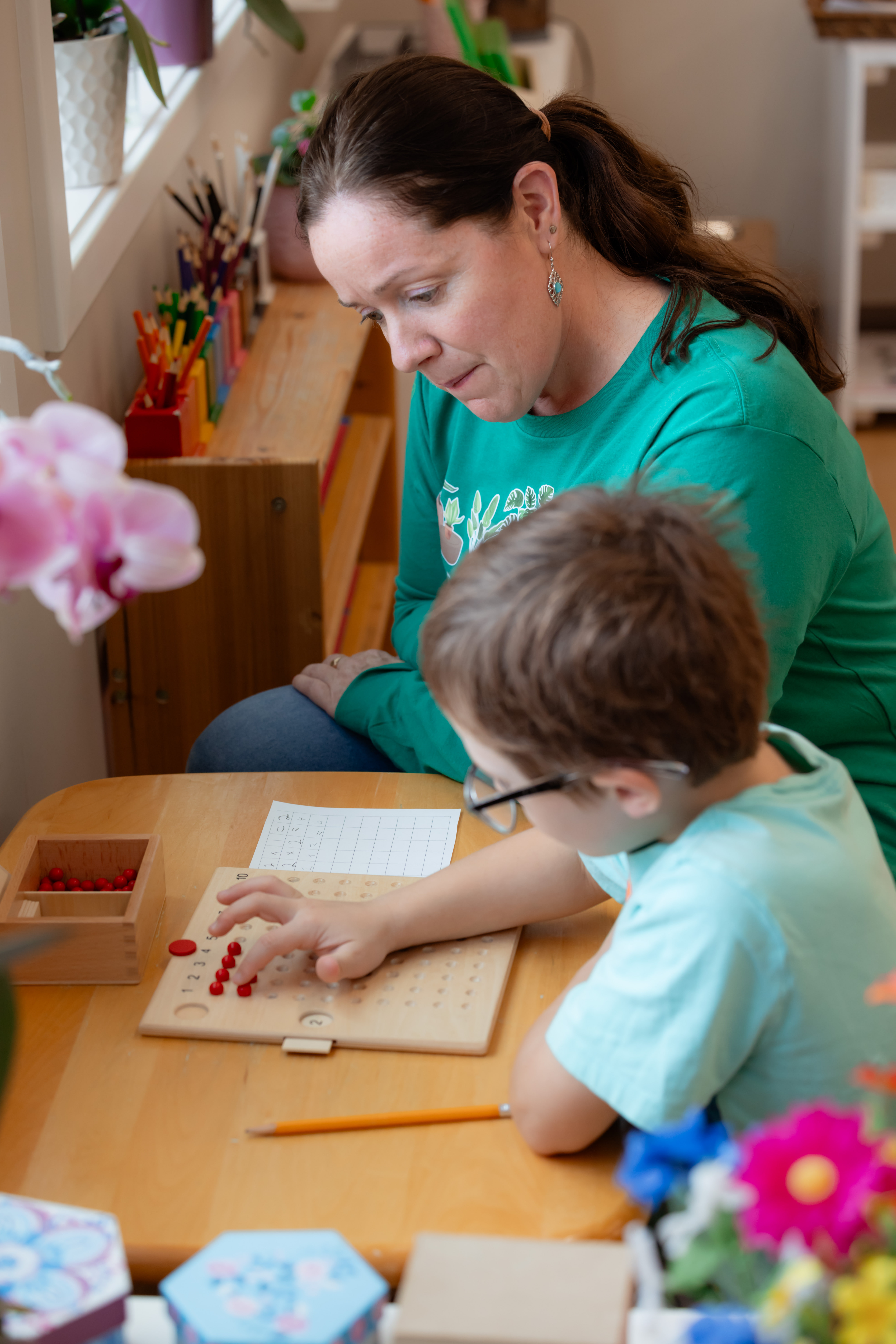 A Montessori Guide observes a young student doing math in a classroom