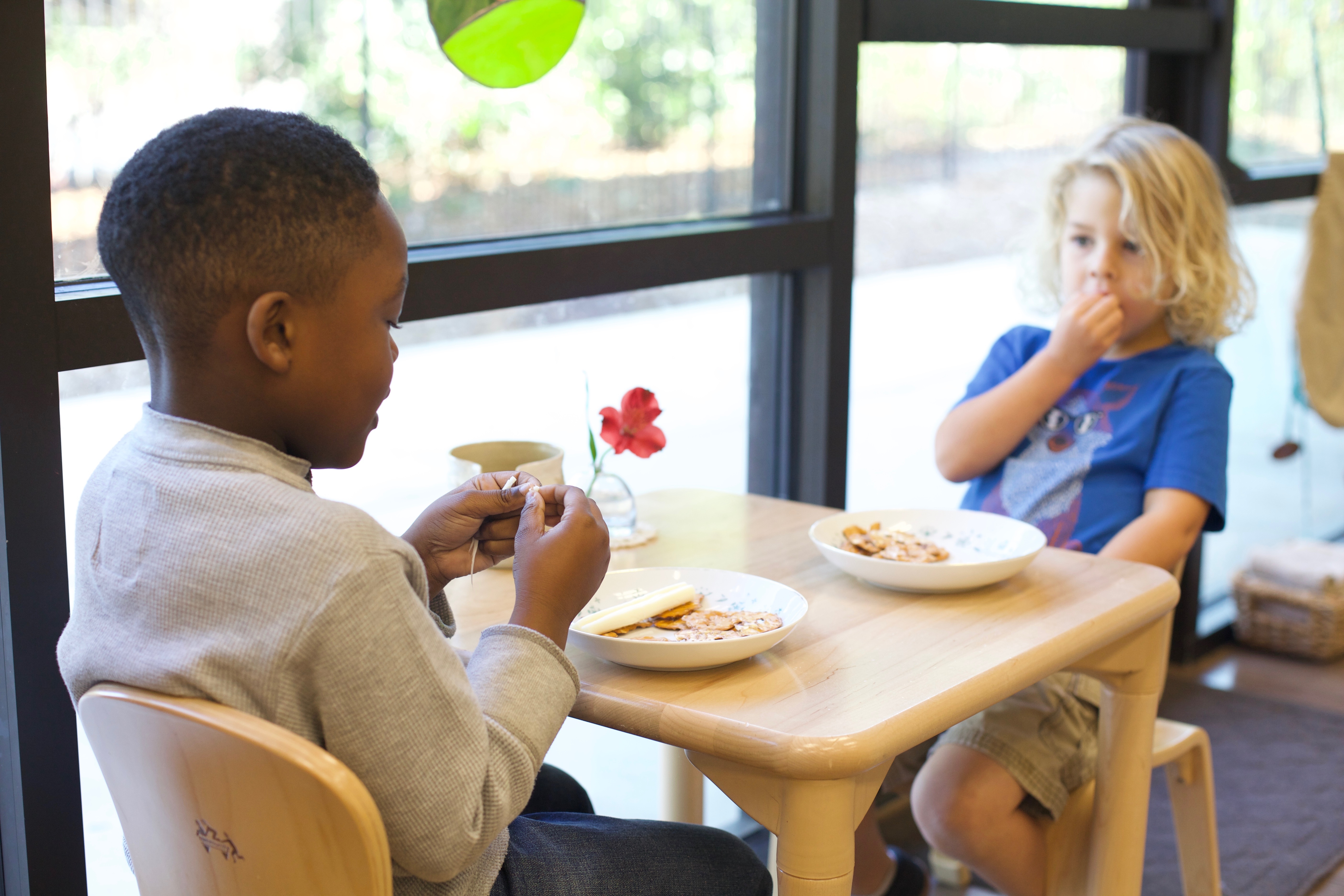 Two Primary children sit at a snack table and eat together in a classroom