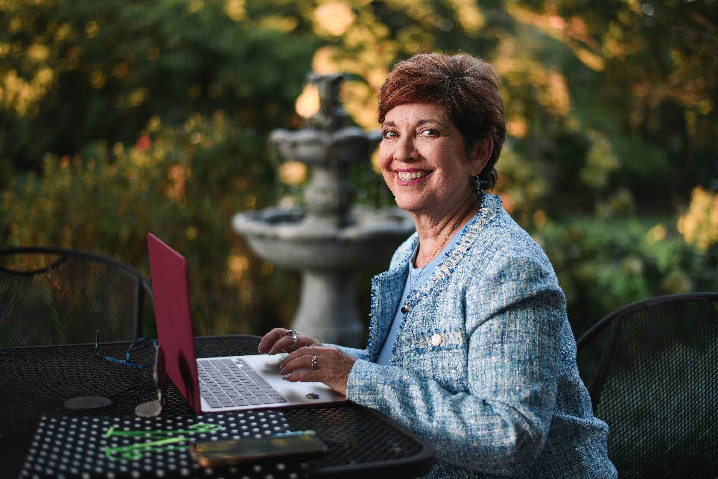 MaryAnn Molloy smiling at her laptop in the garden, writing