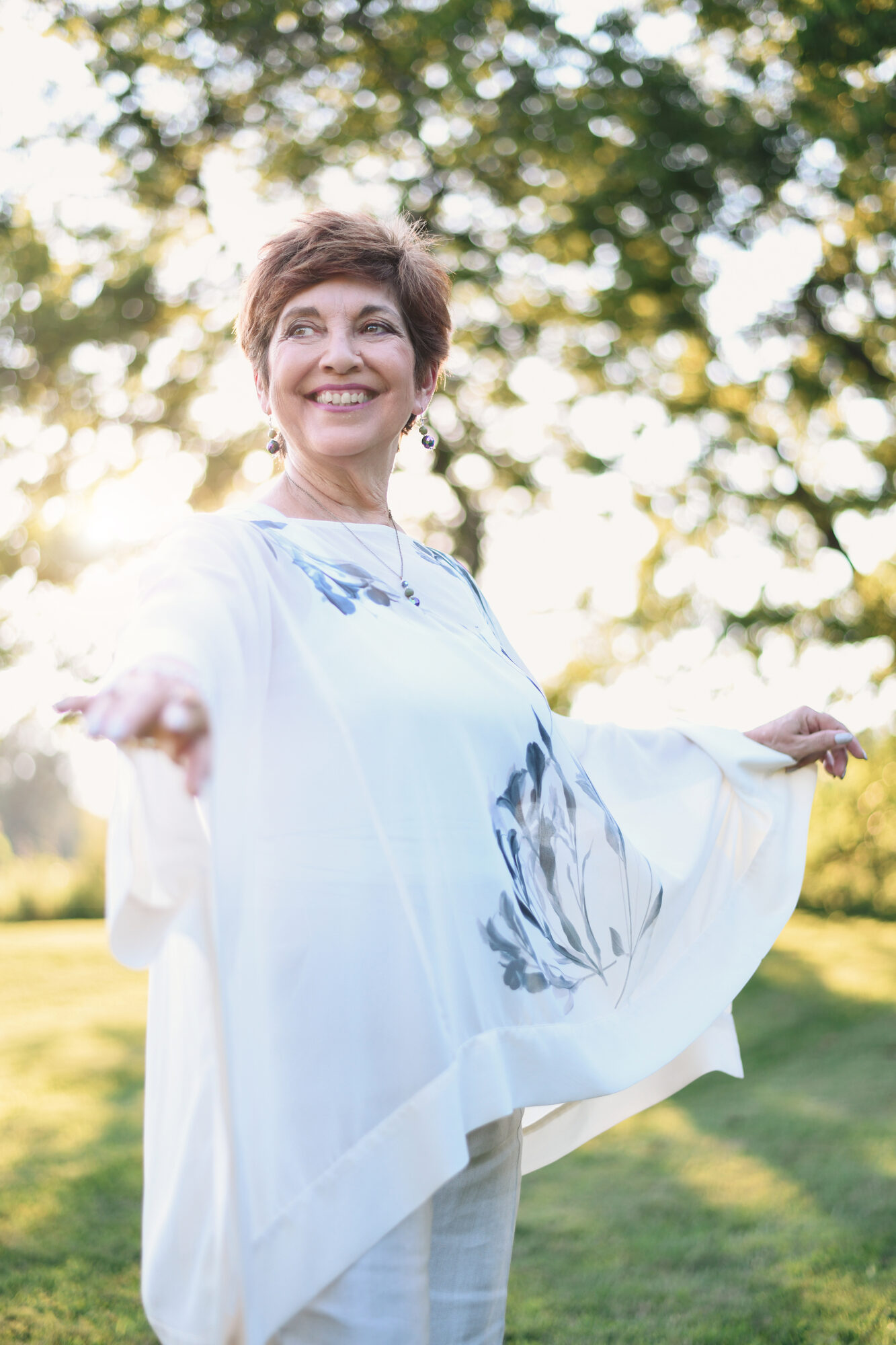 MaryAnn Molloy outdoors in the sunlight, arms open wide