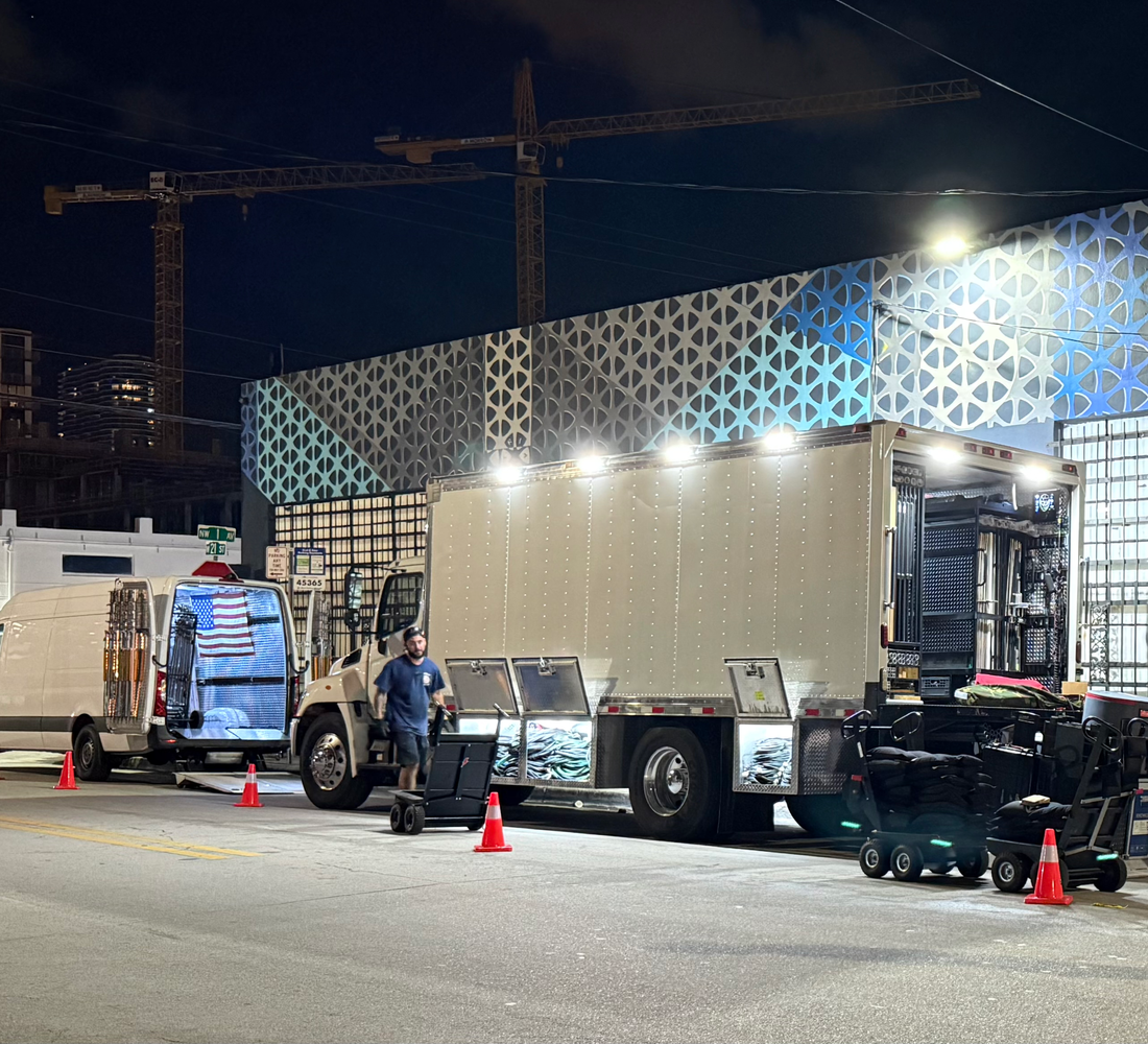 Elevate grip truck at night with its side bins open, a crew member rolling out gear carts