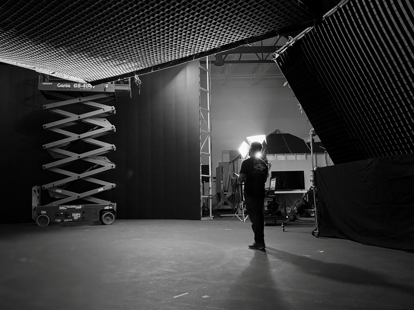 Black and white view of a virtual production stage: a scissor lift and crew under a rigged ceiling grid