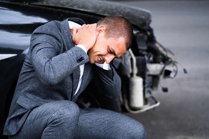 man next to his car feeling pain in his neck after an accident