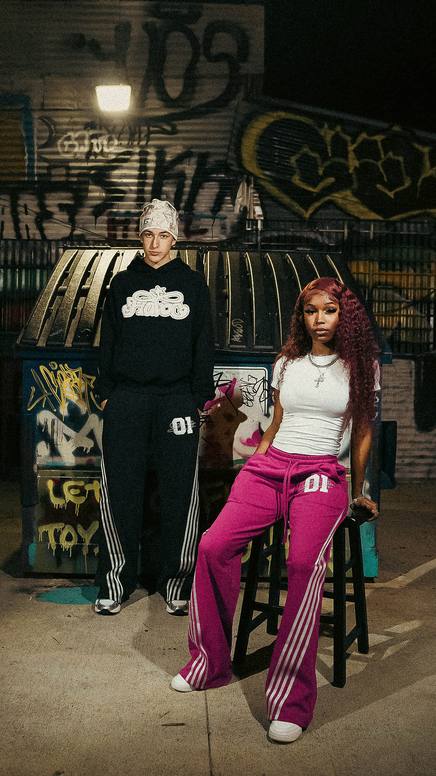 Two models in tracksuits at a graffiti wall