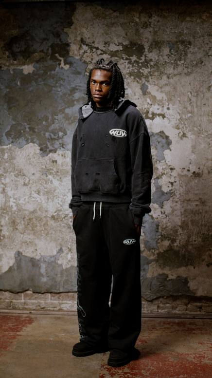 Model in a black hoodie and sweats against a textured wall