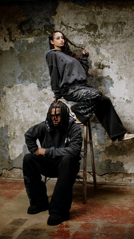 Two models in Wish U Well outerwear against a weathered wall