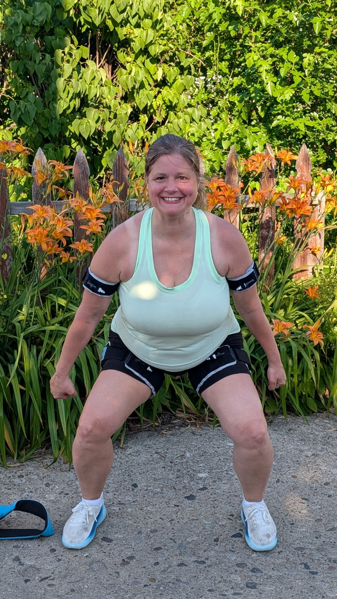 Lori Diamos performing a squat while wearing B3 Blood Flow Restriction bands outdoors in her garden, demonstrating functional lower body strength training. Lori Diamos performing a squat while wearing B3 Blood Flow Restriction bands outdoors in her garden, demonstrating functional lower body strength training.