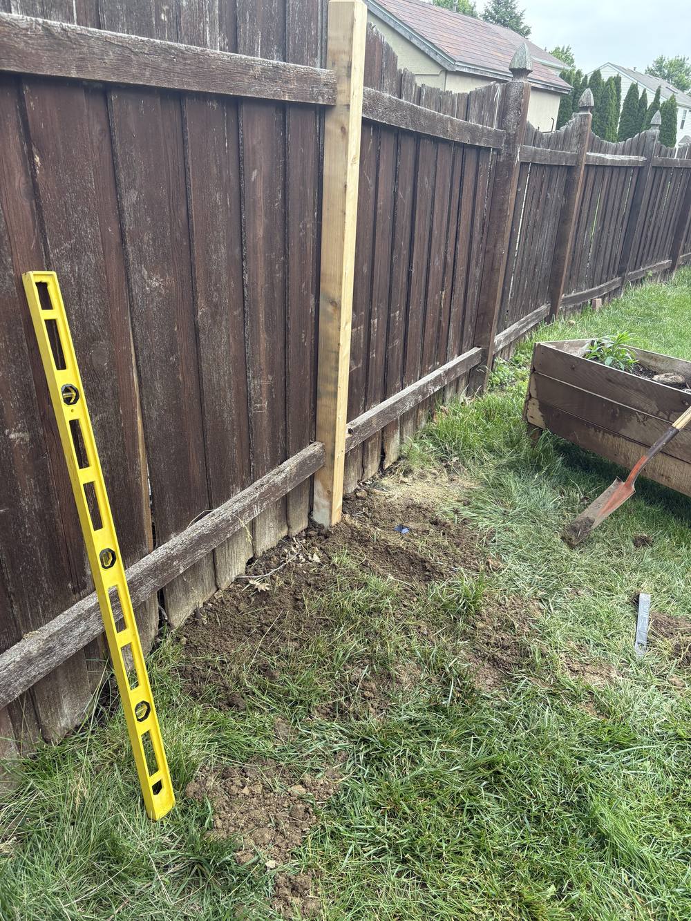 New fence post being set plumb and level next to an existing fence