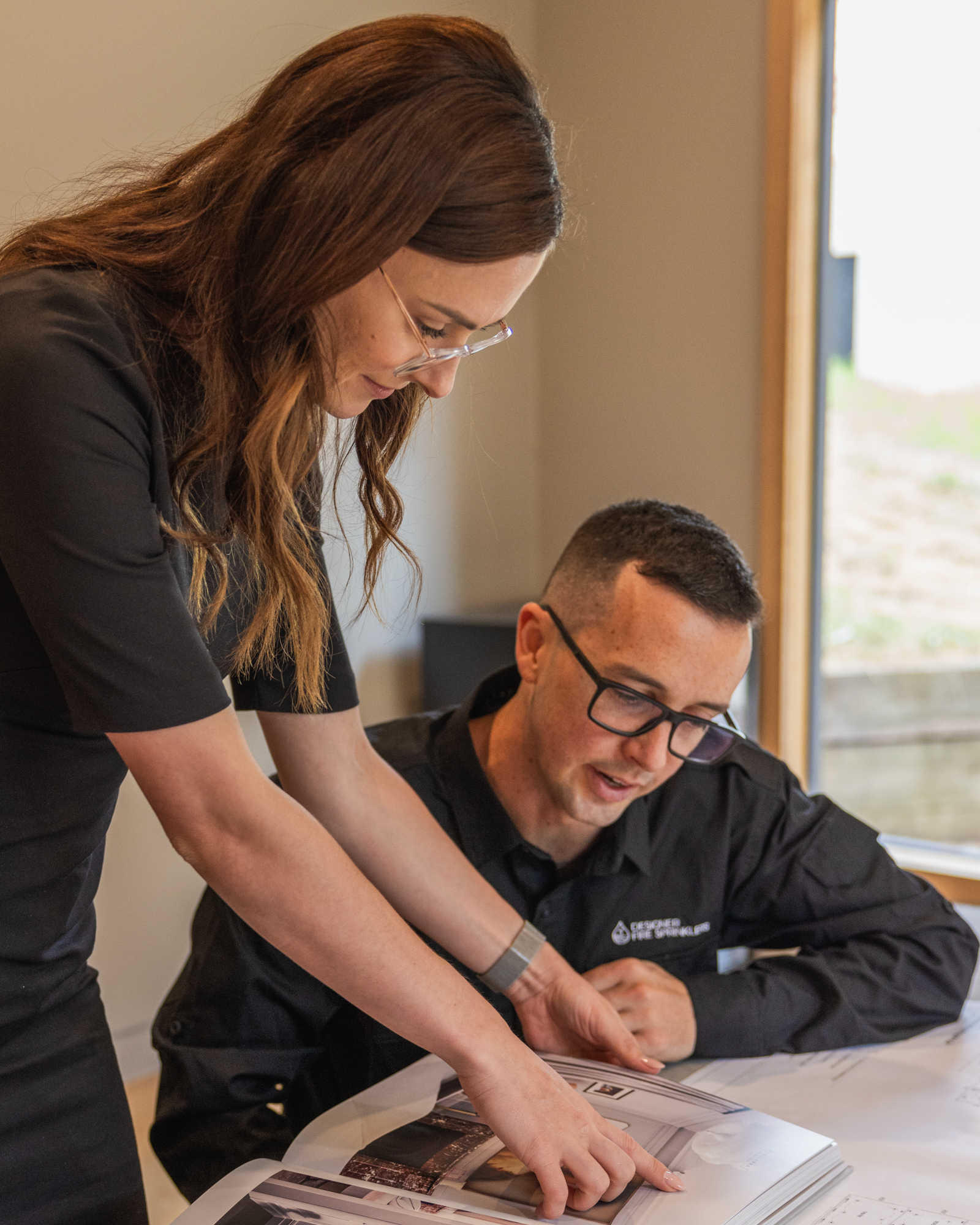 Raph seated and Sionainn pointing at a magazine during a Designer Fire Sprinklers photoshoot