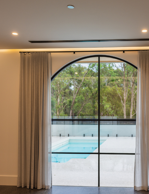 Modern room with tall glass windows, pool view, and black fire sprinkler on a beige ceiling