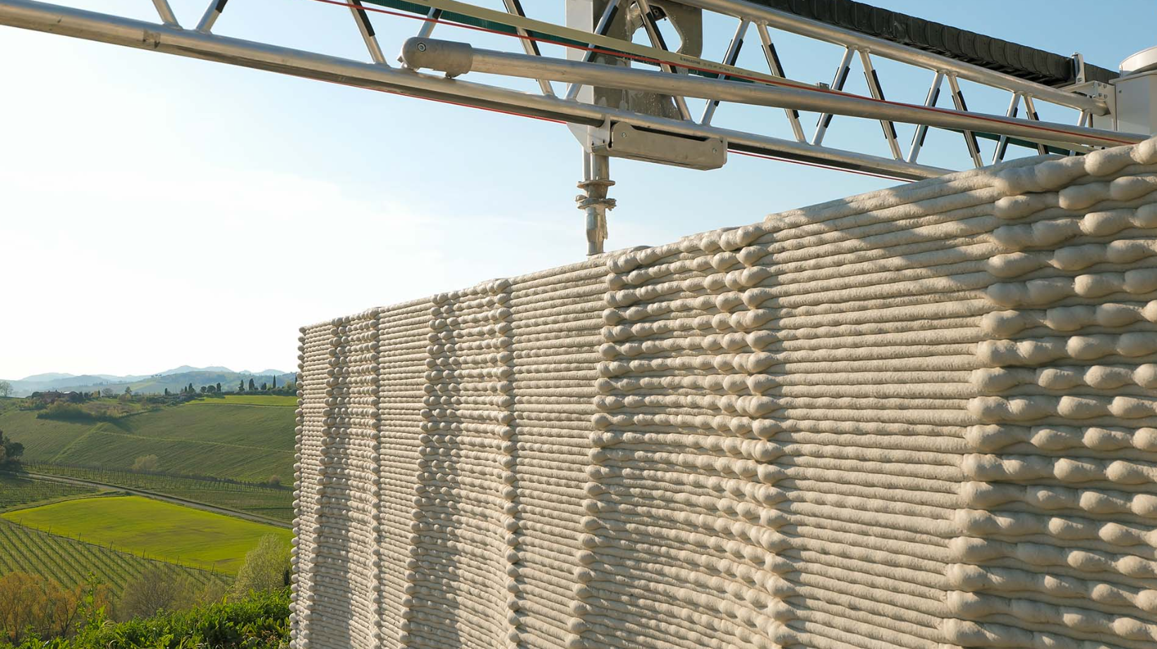 Close-up of a large-scale 3D printer constructing earth-based bioconstruction walls using natural materials for sustainable regenerative architecture and low-carbon housing.