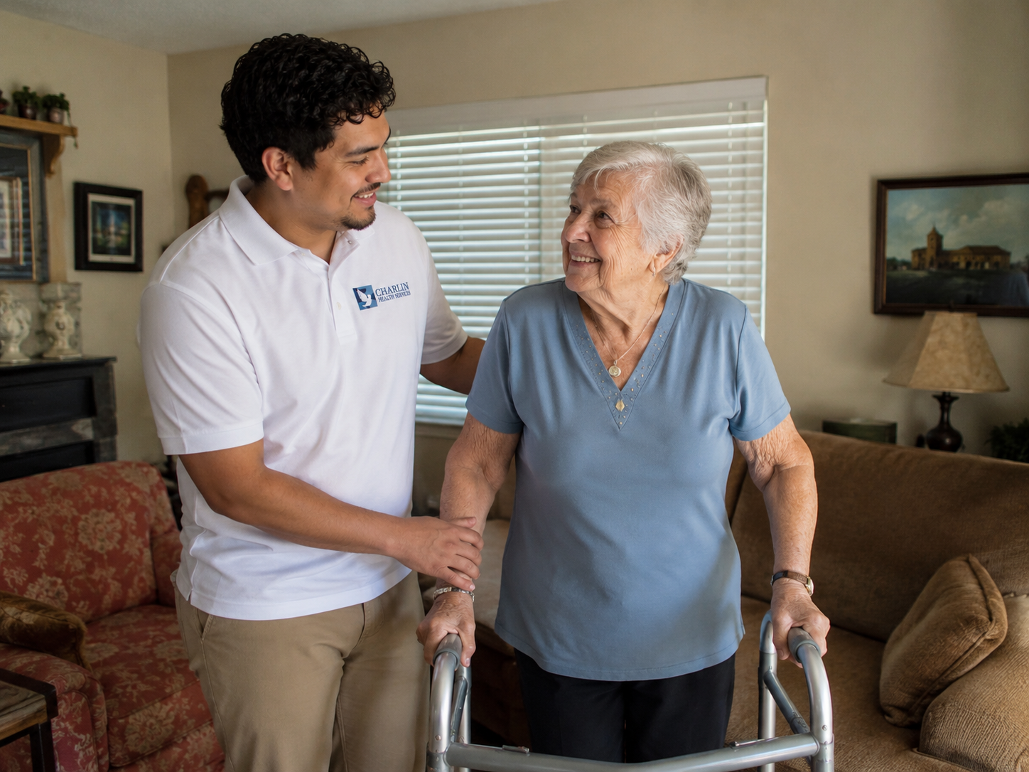 A caregiver sitting with an older woman in a bright living room, holding her hand