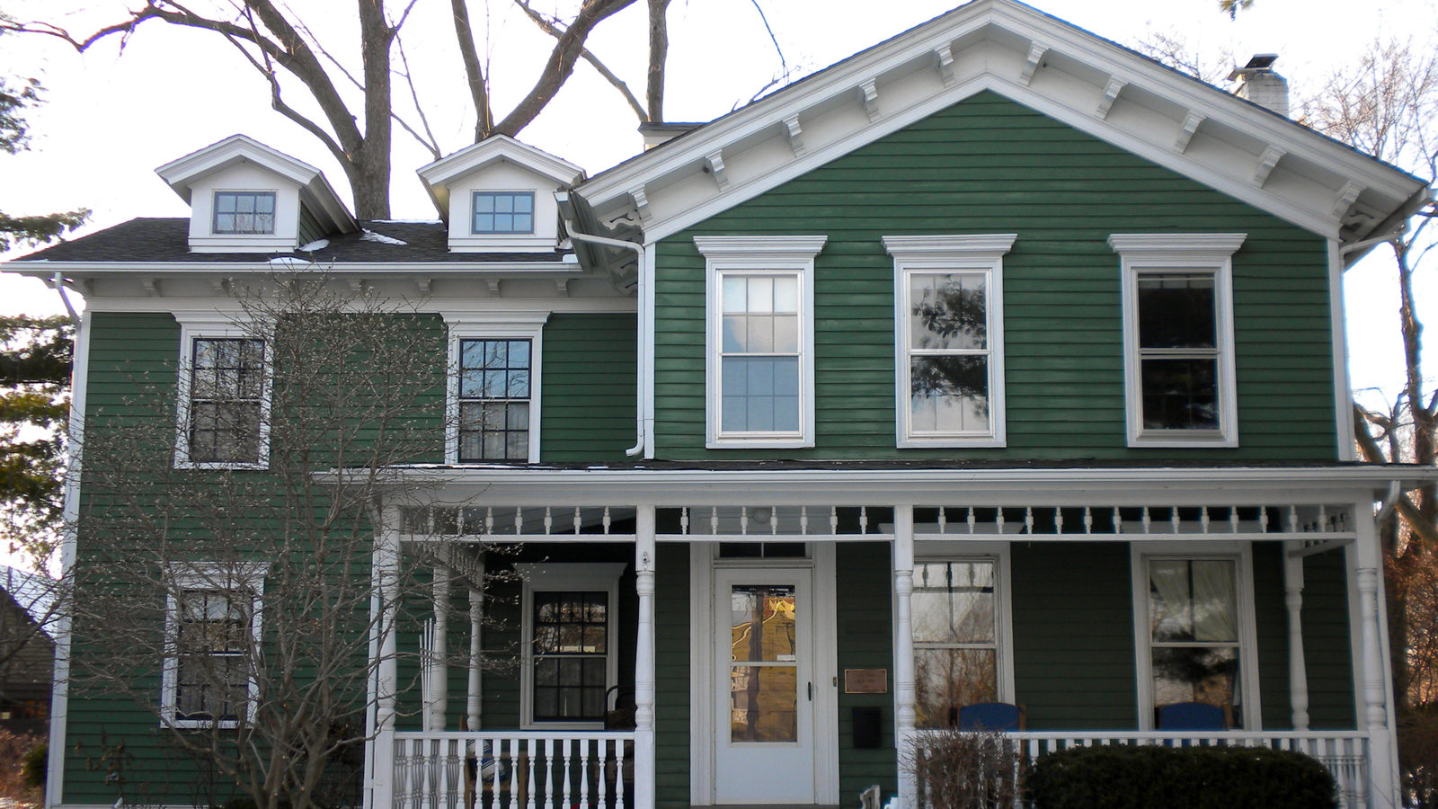 Green two-story historic house with white trim and a front porch in Geneva, Illinois