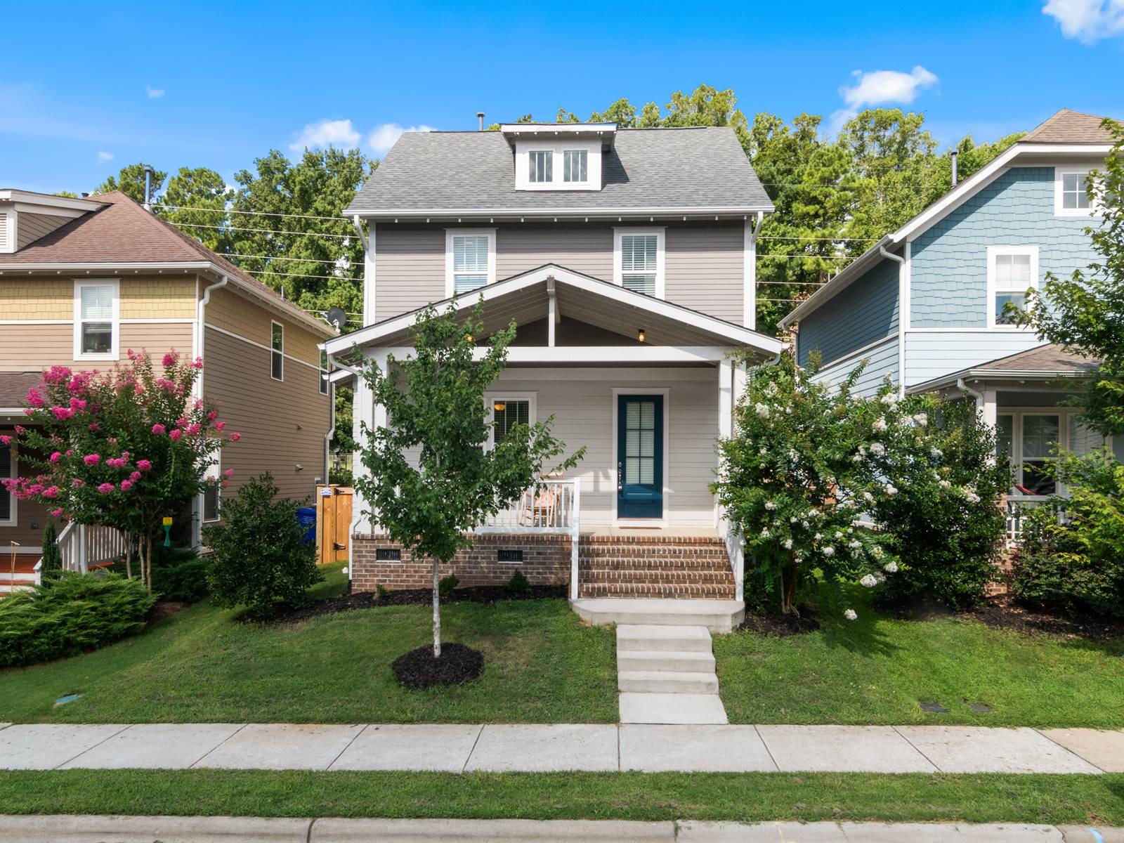 Two-story house with a covered front porch and brick steps on a tree-lined residential street