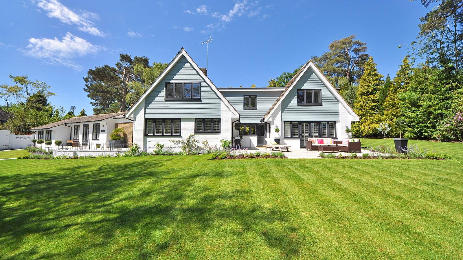 Light brick suburban house with large lawn and patio furniture under blue sky