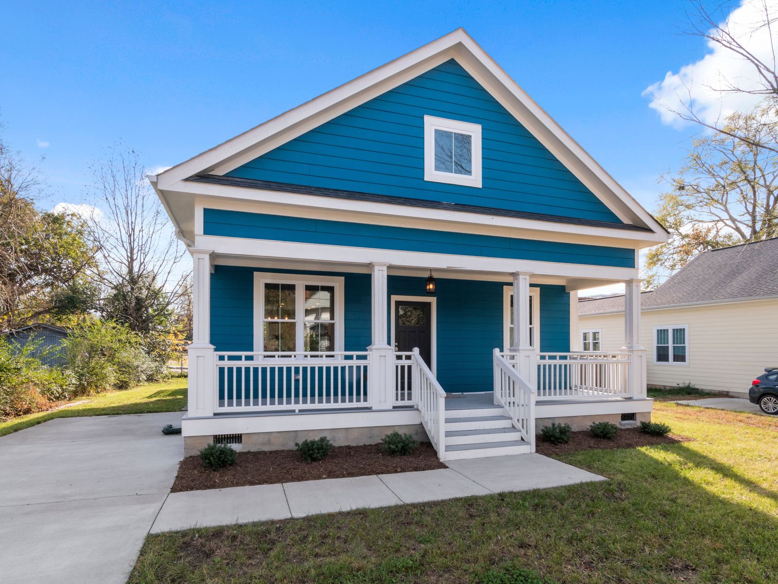 Blue house with a gabled roof and a white front porch on a sunny residential street