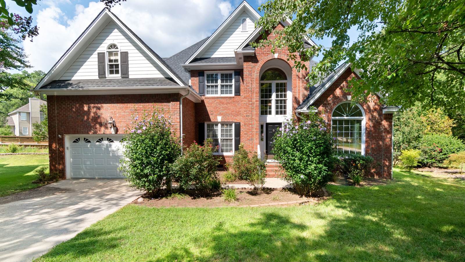 Two-story brick house with an attached garage and a green front lawn