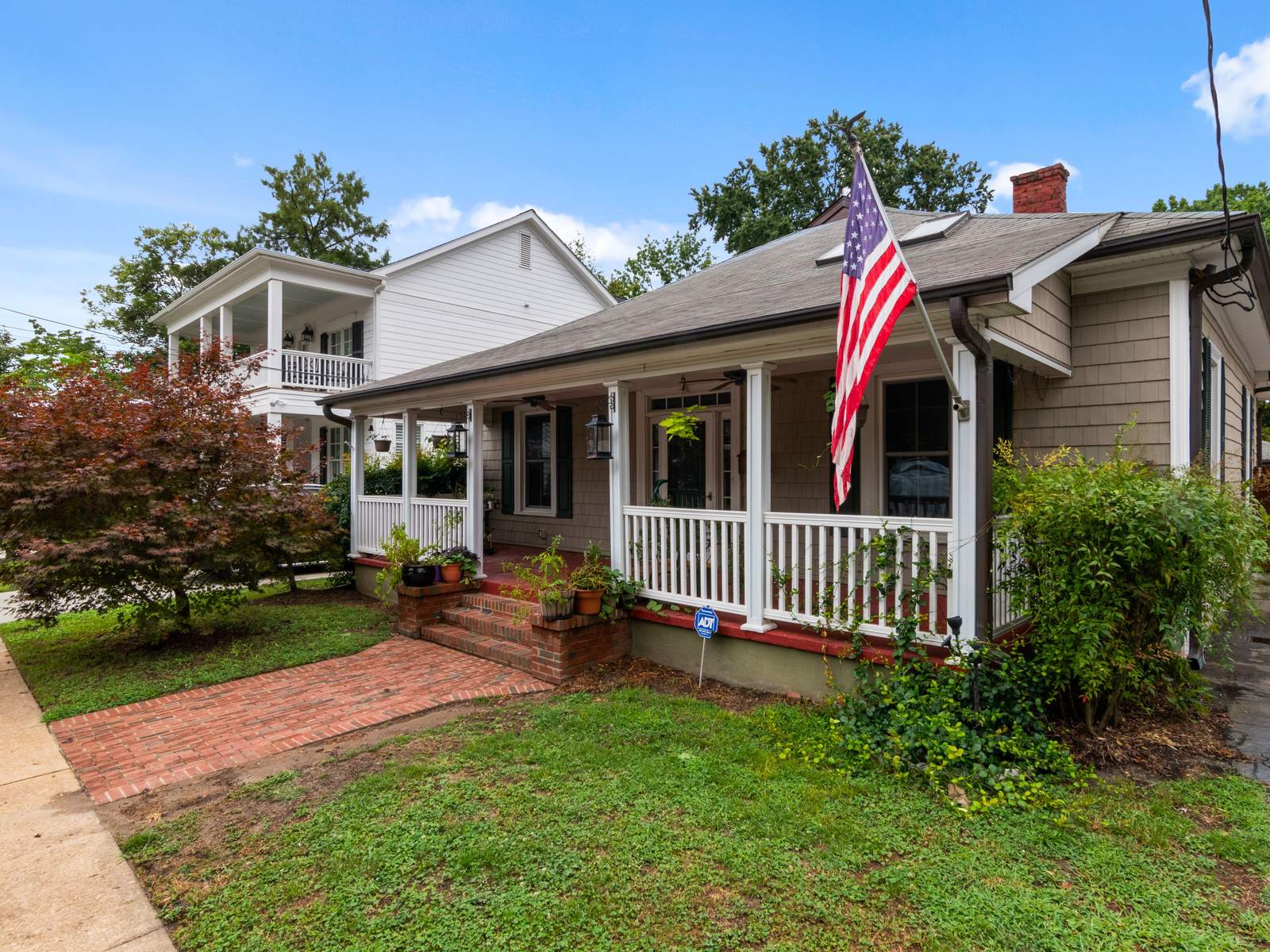 Older bungalow with a white front porch, a brick walk and an American flag