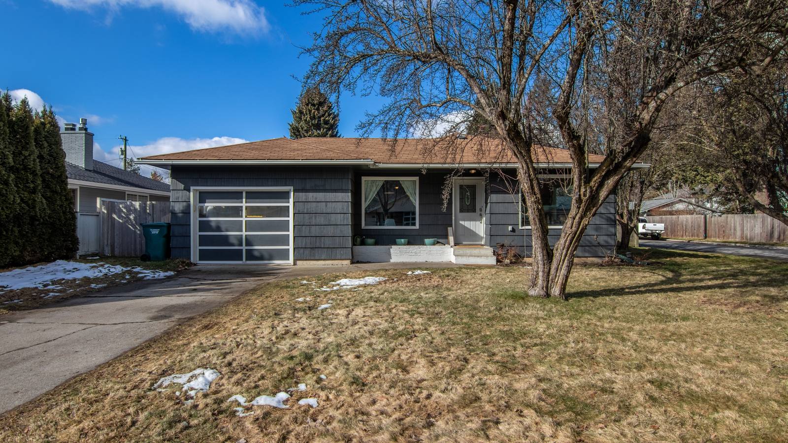 Single-story ranch house with a garage and a bare tree in a late-winter front yard