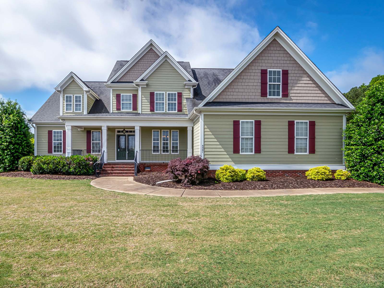 Two-story house with a covered front porch, red shutters and a wide front lawn