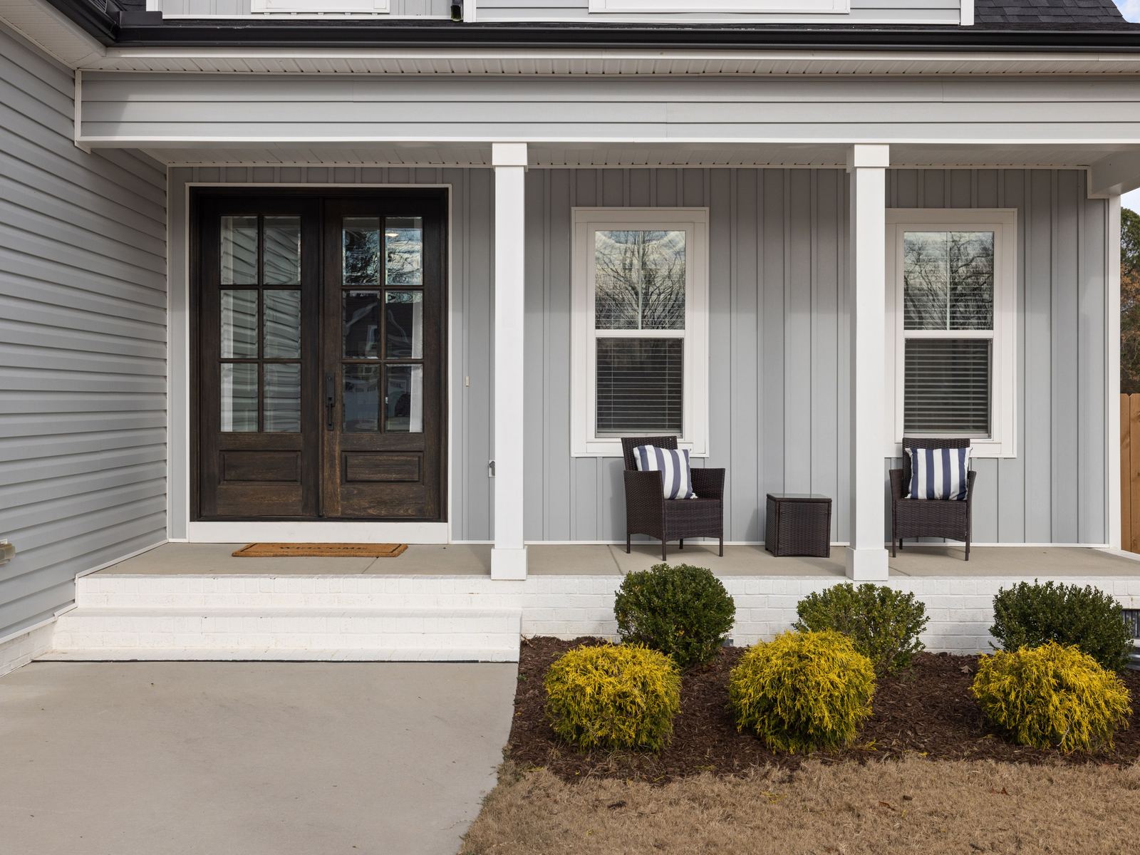Covered front porch with two chairs, white columns and a dark front door