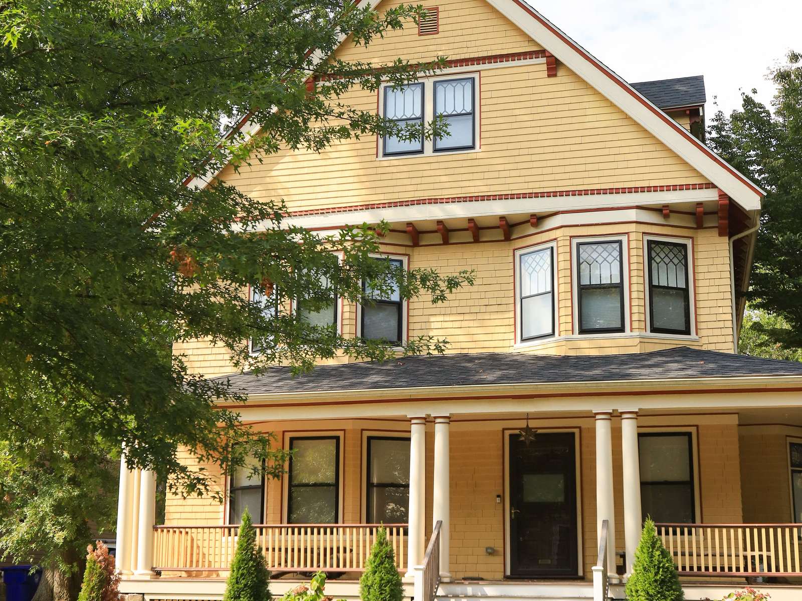Yellow two-story house with a wide covered front porch and white columns on a tree-lined street