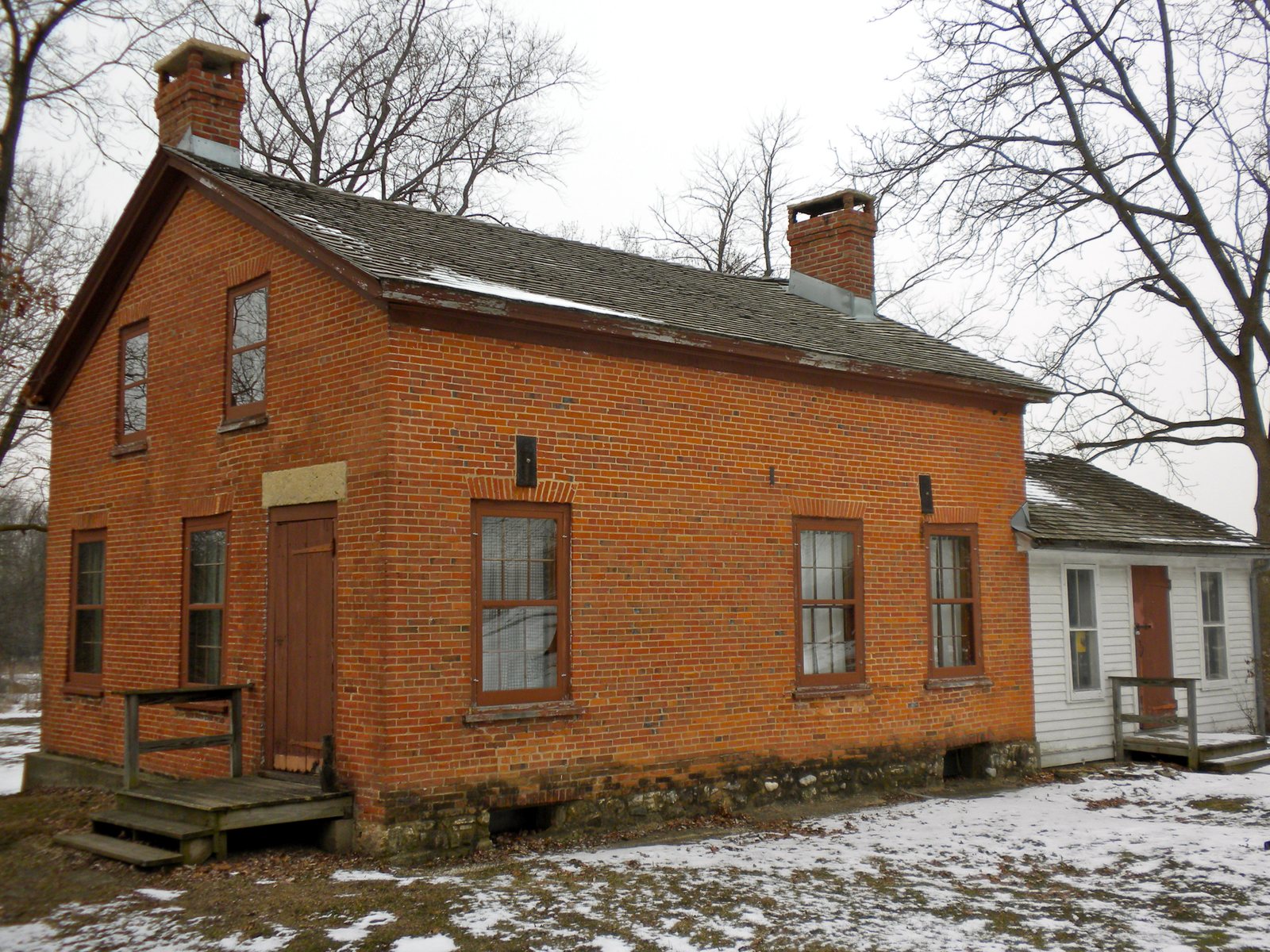Old red brick farmhouse with a small white wing, in a Kane County forest preserve in winter