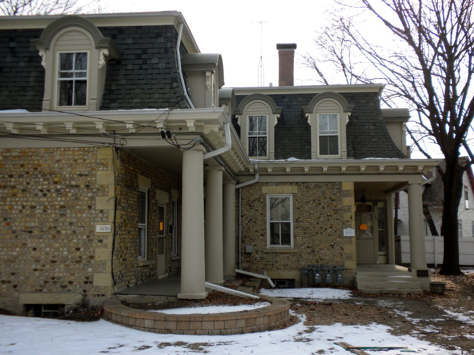 A large stone house with a wide columned porch and a dark mansard roof in Elgin, Illinois, in winter