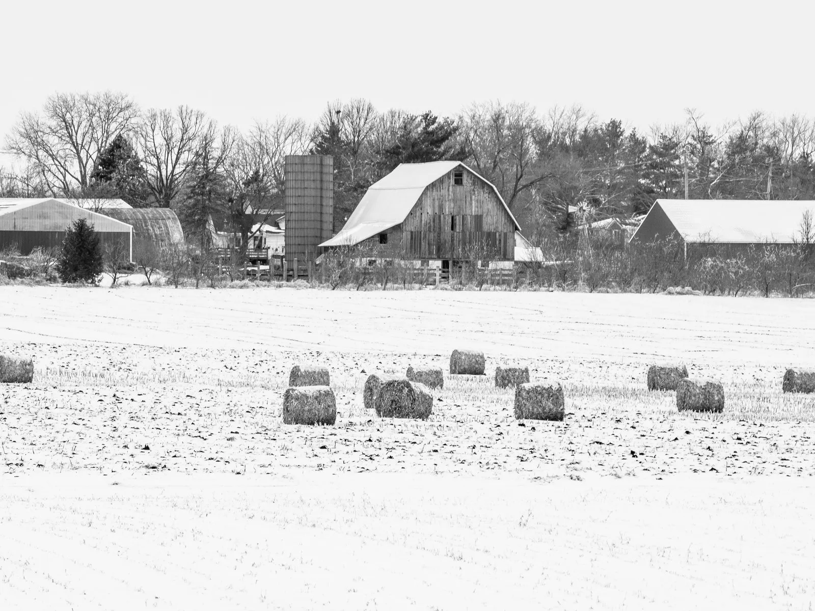 A farm with barns, a silo and hay bales in a snow-covered field in Kane County, Illinois