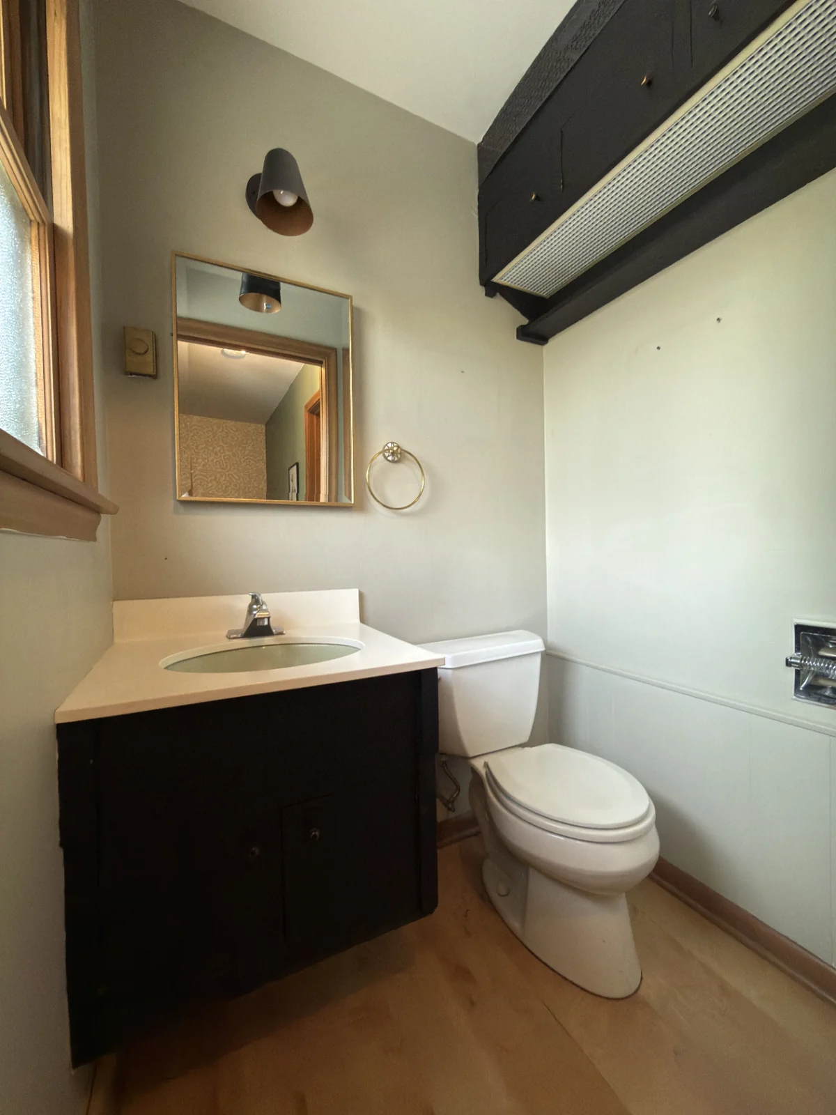 Bathroom before remodel: dated dark vanity, worn flooring, exposed soffit.