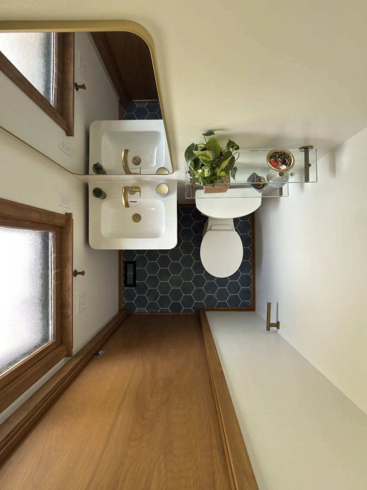 Bathroom after remodel, wide view: navy hexagon tile, brass hardware, floating sink, glass shelf styling.