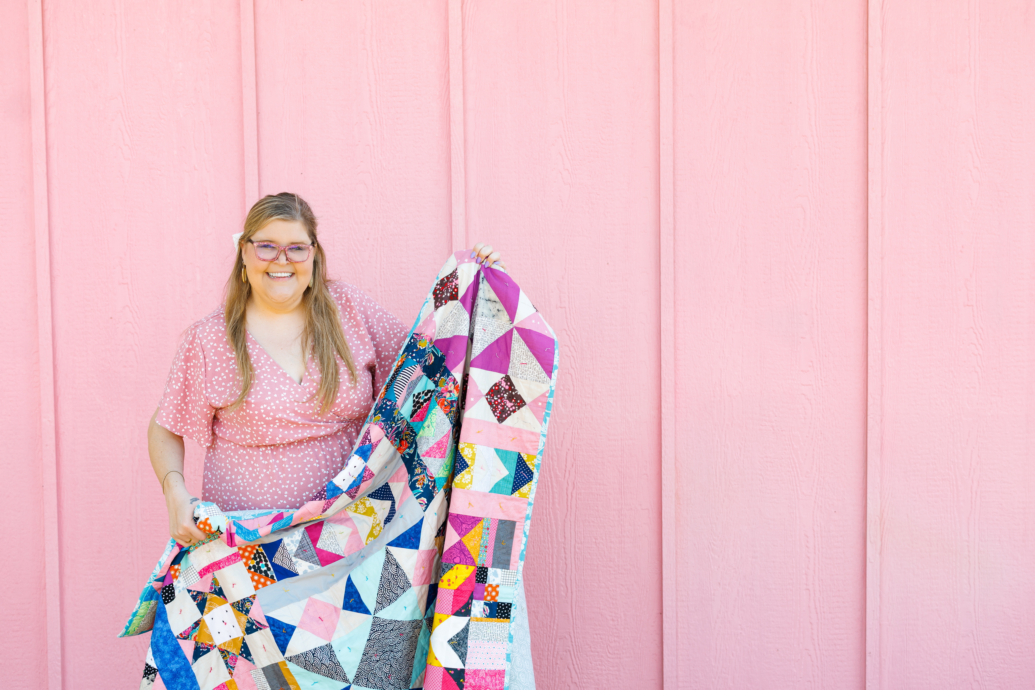 Christen laughing and holding up a scrappy star quilt against a pink wall