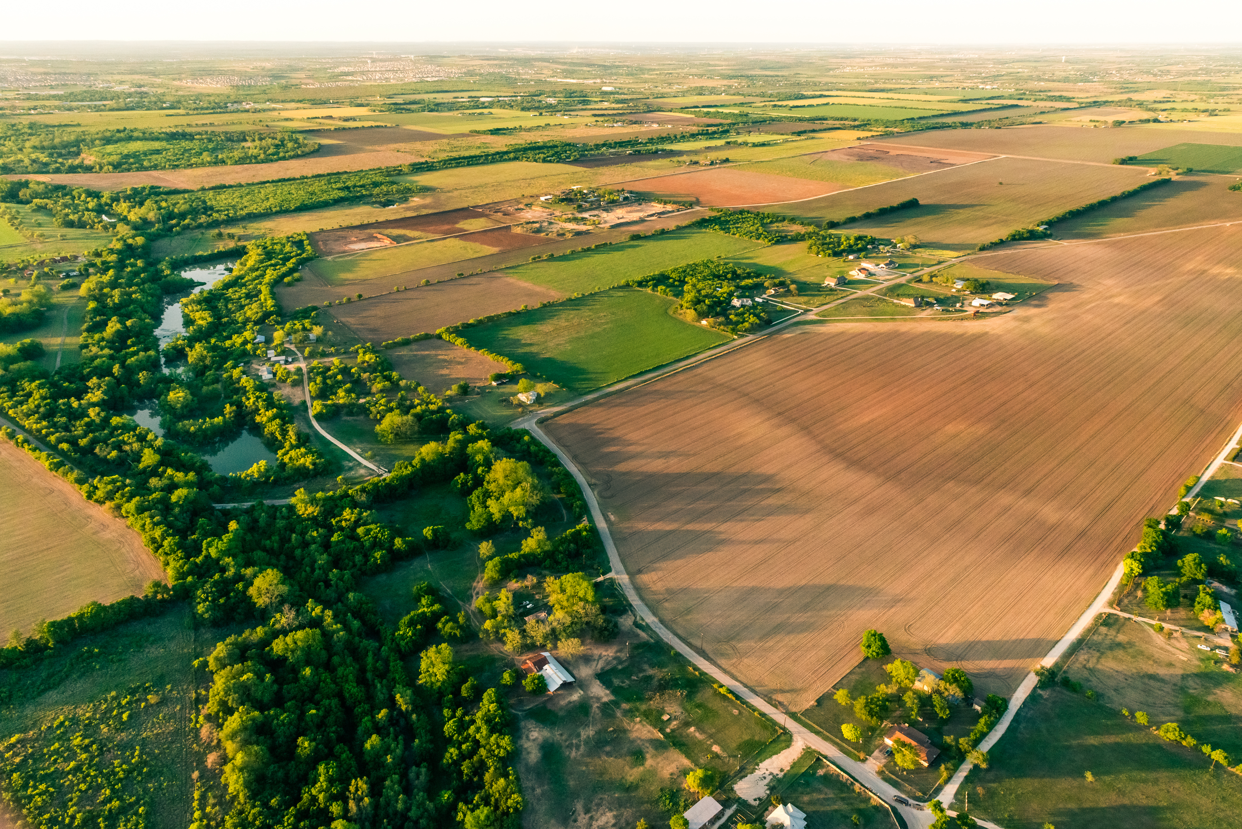Aerial view of rural acreage with farm fields, tree lines, roads and scattered homes