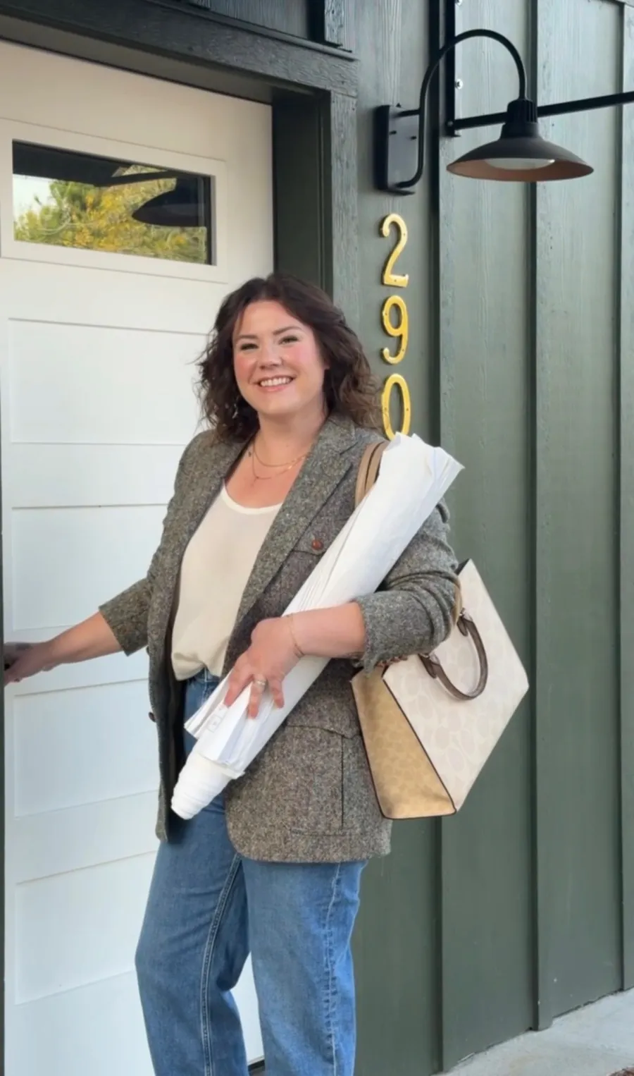Kelsie, Raspberry & Oak developer, at a front door holding rolled blueprints