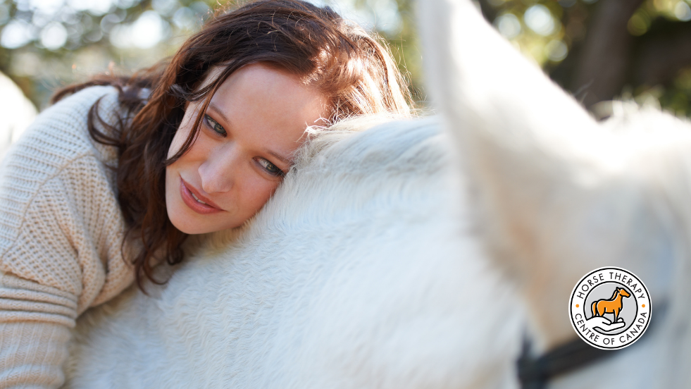 Woman resting her head on a horse during therapy experience Woman resting her head on a horse during therapy experience