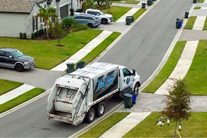 A Titan Trash truck picking up curbside bins along a residential street for trash service tucson.