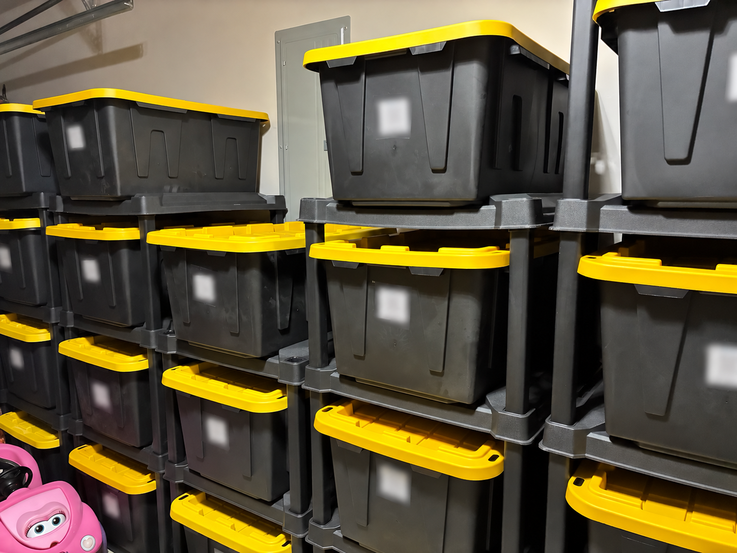 My garage storage racks holding black bins with yellow lids; all visible inventory labels are heavily blurred for privacy.