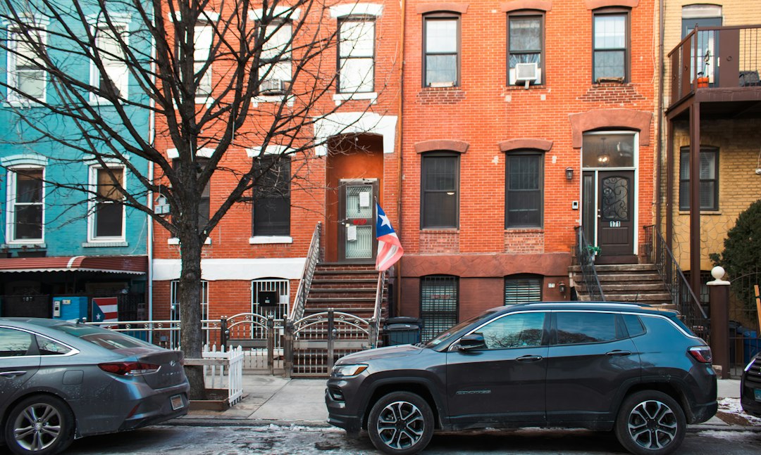 Brooklyn brick and painted rowhouses with stoops along a residential street, parked cars at the curb, bare winter tree.