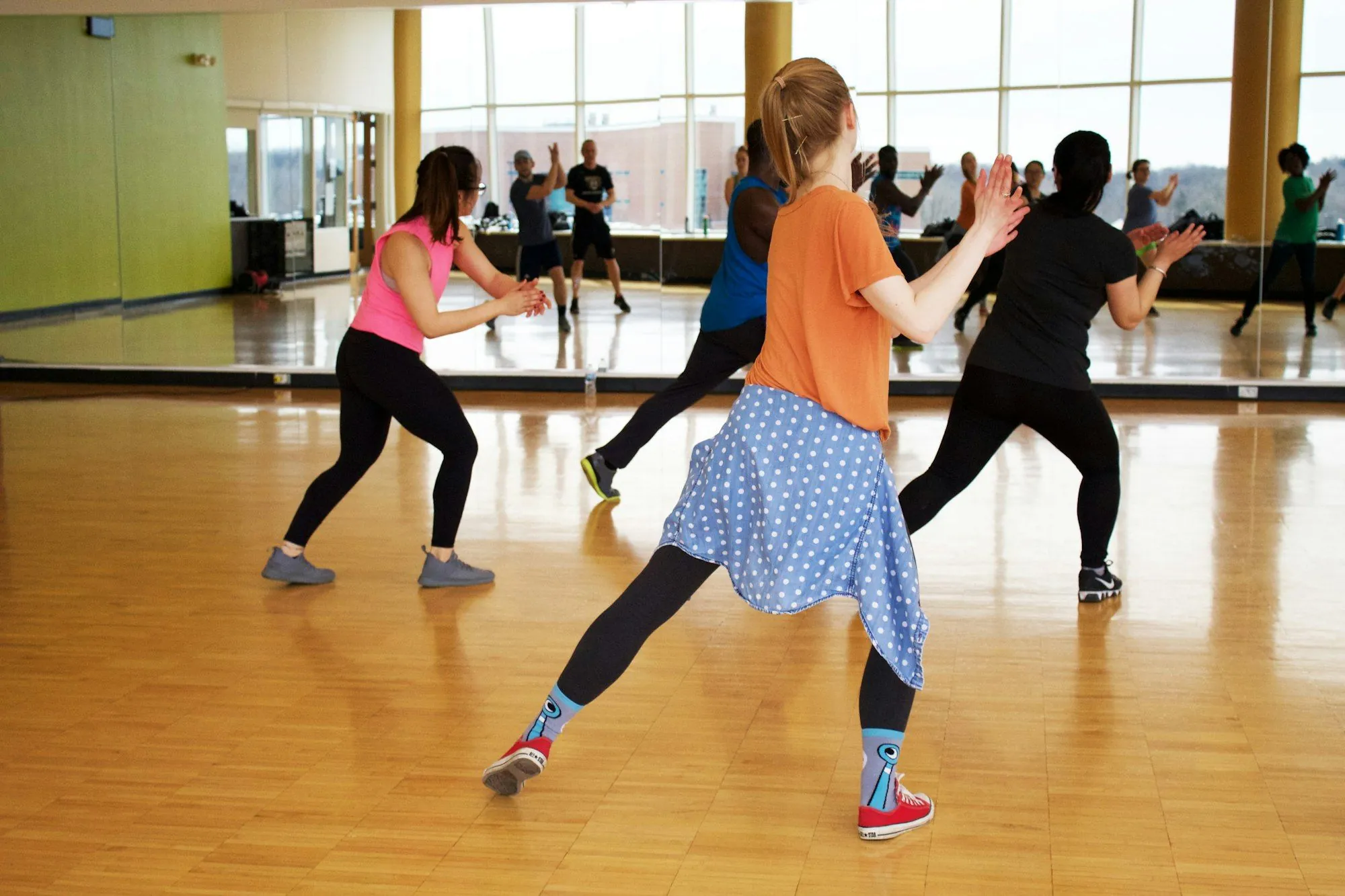 Dancers mid-routine across a bright studio floor with a mirror wall