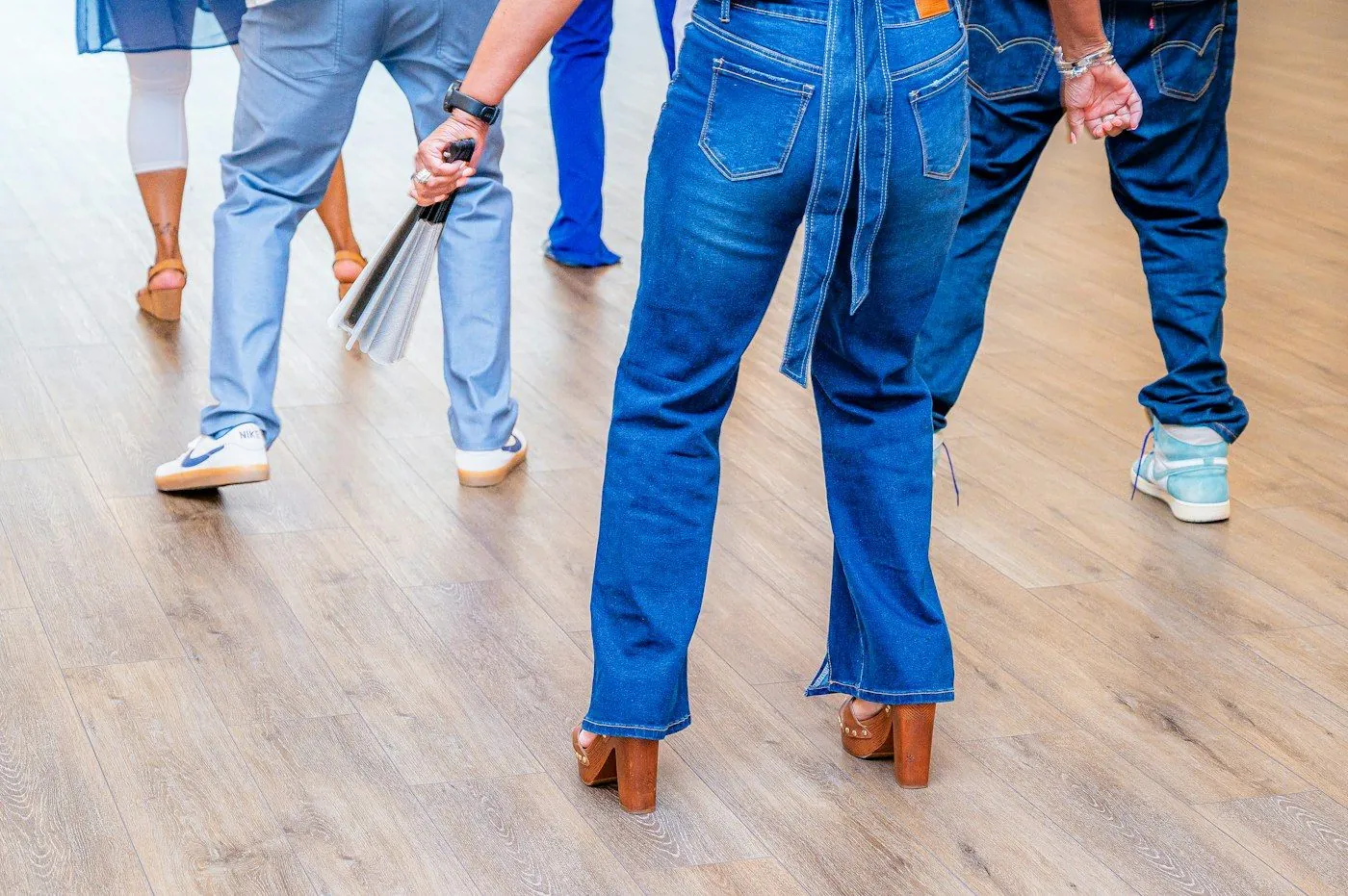 A group of adult beginners in jeans and sneakers learning steps on a wood floor