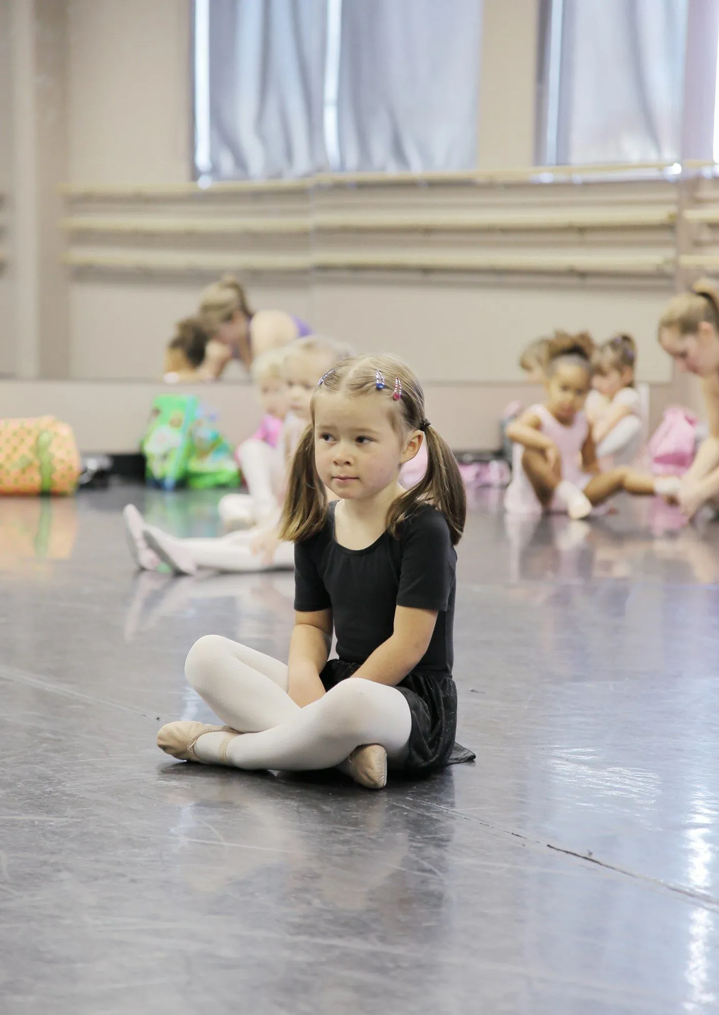 A young girl sitting on a studio floor during a kids dance class