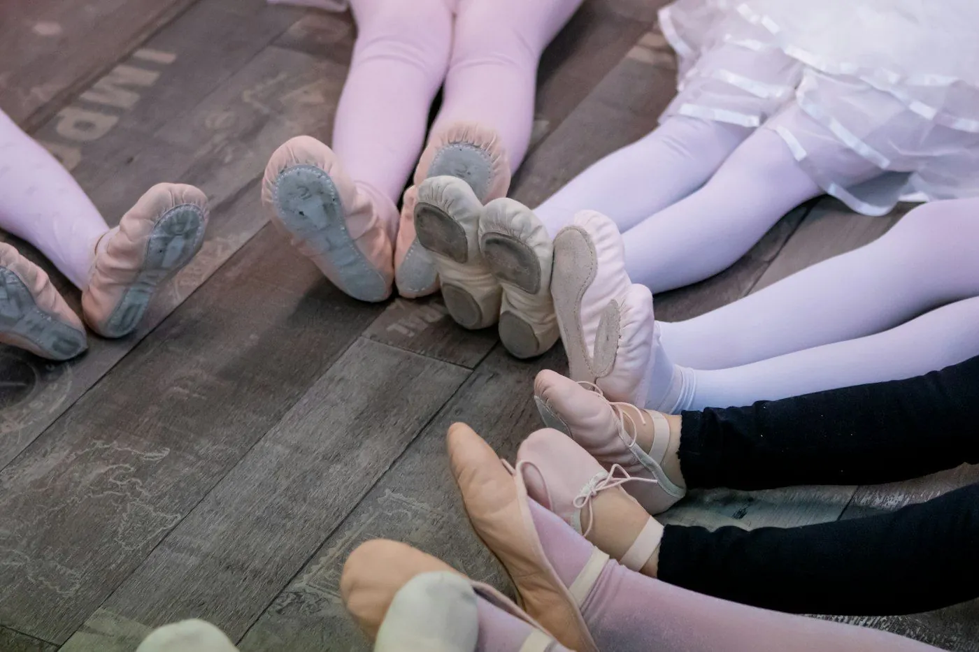 Young dancers in ballet slippers sitting in a row on the studio floor