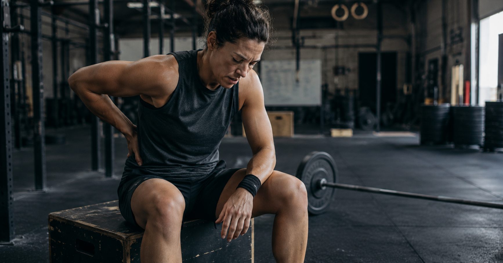 CrossFit athlete sitting on plyo box during rest holding lower back, pain and determination, Las Vegas NV chiropractic care