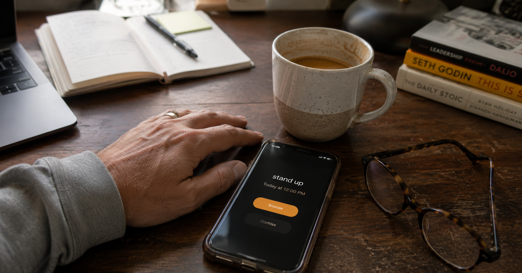 hand resting on a desk beside a phone alarm reminder to stand and move hand resting on a desk beside a phone alarm reminder to stand and move