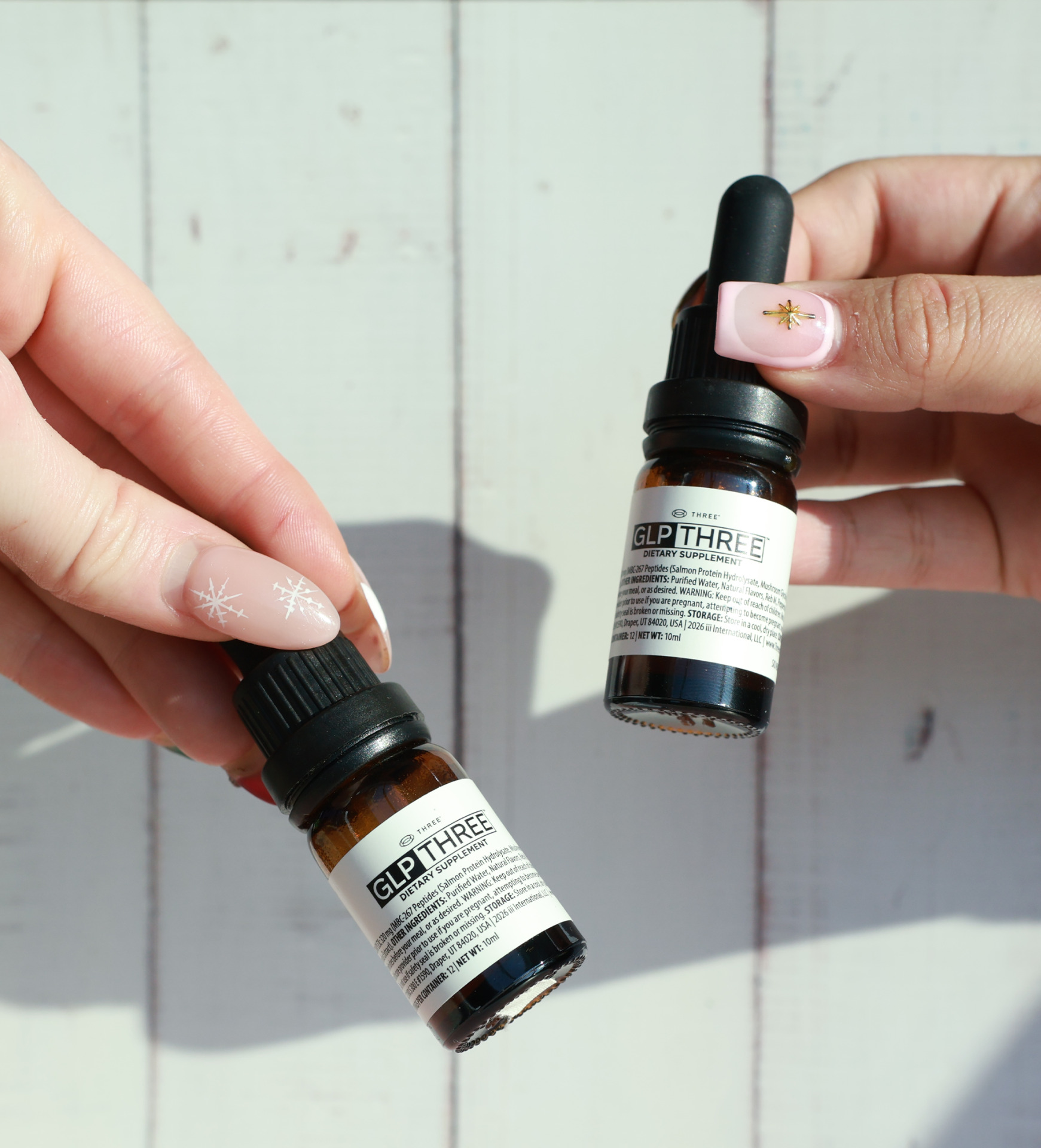 Two bottles of GLP THREE natural weight management formula with dropper caps, held in hand